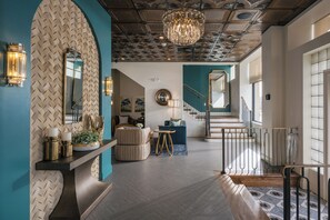A modern interior with a herringbone patterned wall, a chandelier, a staircase, and a round mirror.