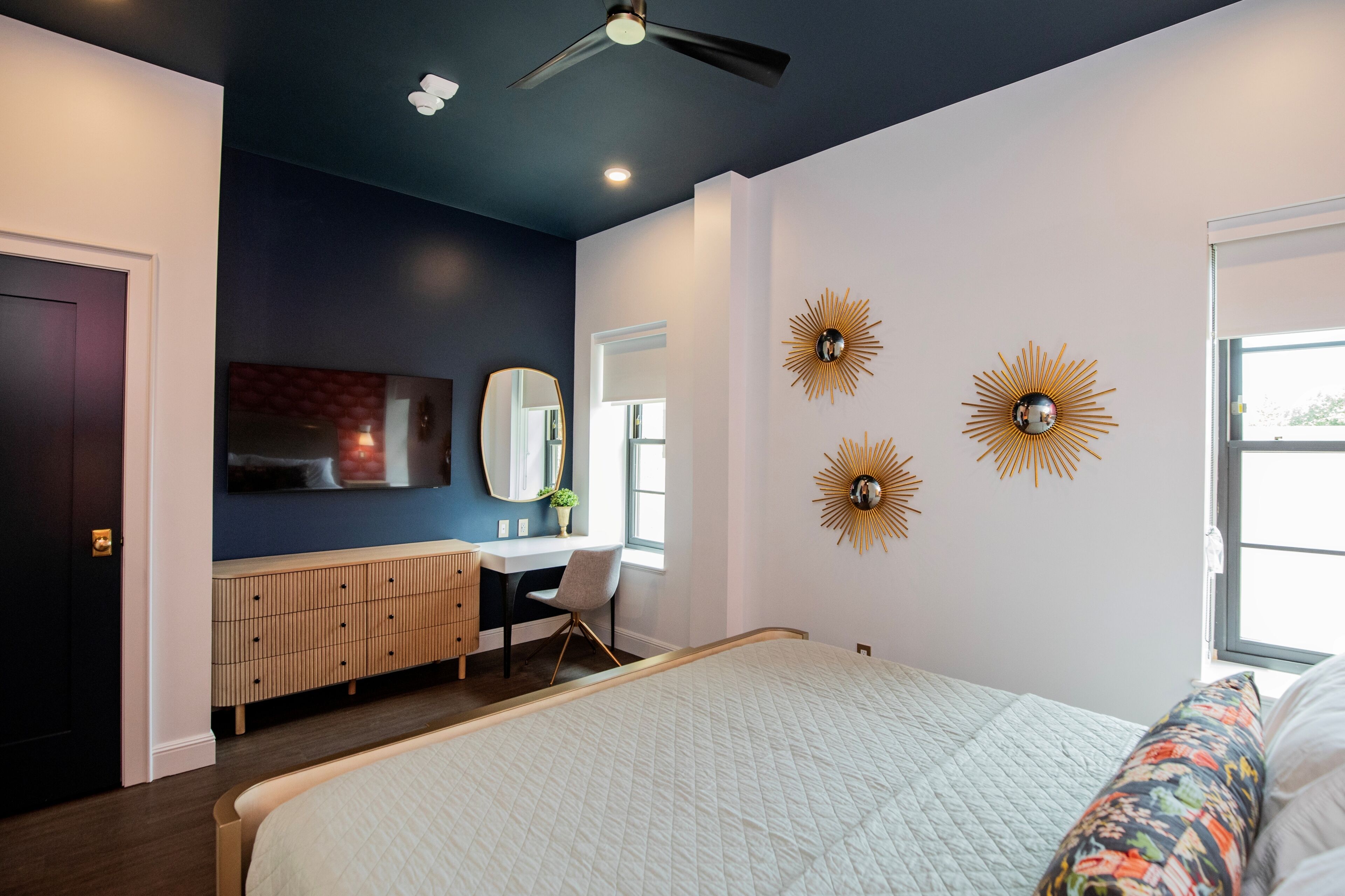 Un dormitorio con cama, escritorio, silla, ventilador de techo y elementos decorativos en la pared.