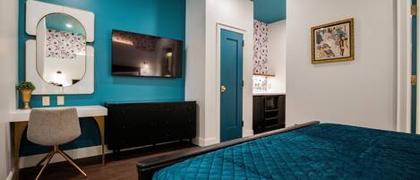 Un dormitorio con cama, escritorio, silla, radiador, puerta y televisor montado en la pared.