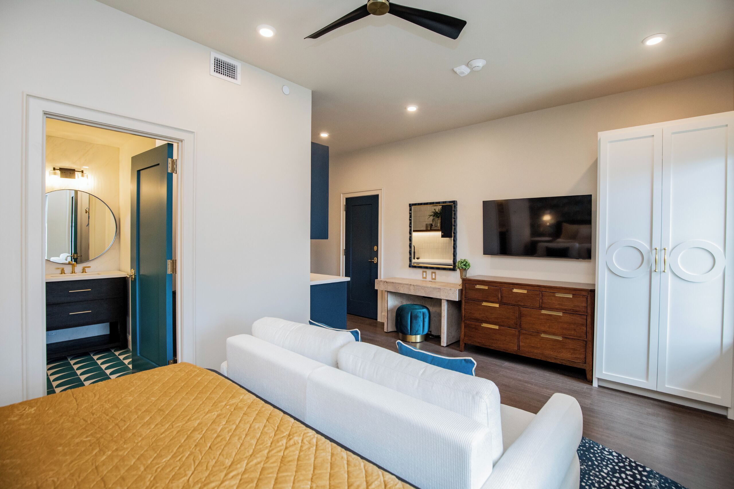 A modern bedroom with a bed, a vanity, a wardrobe, and a ceiling fan.