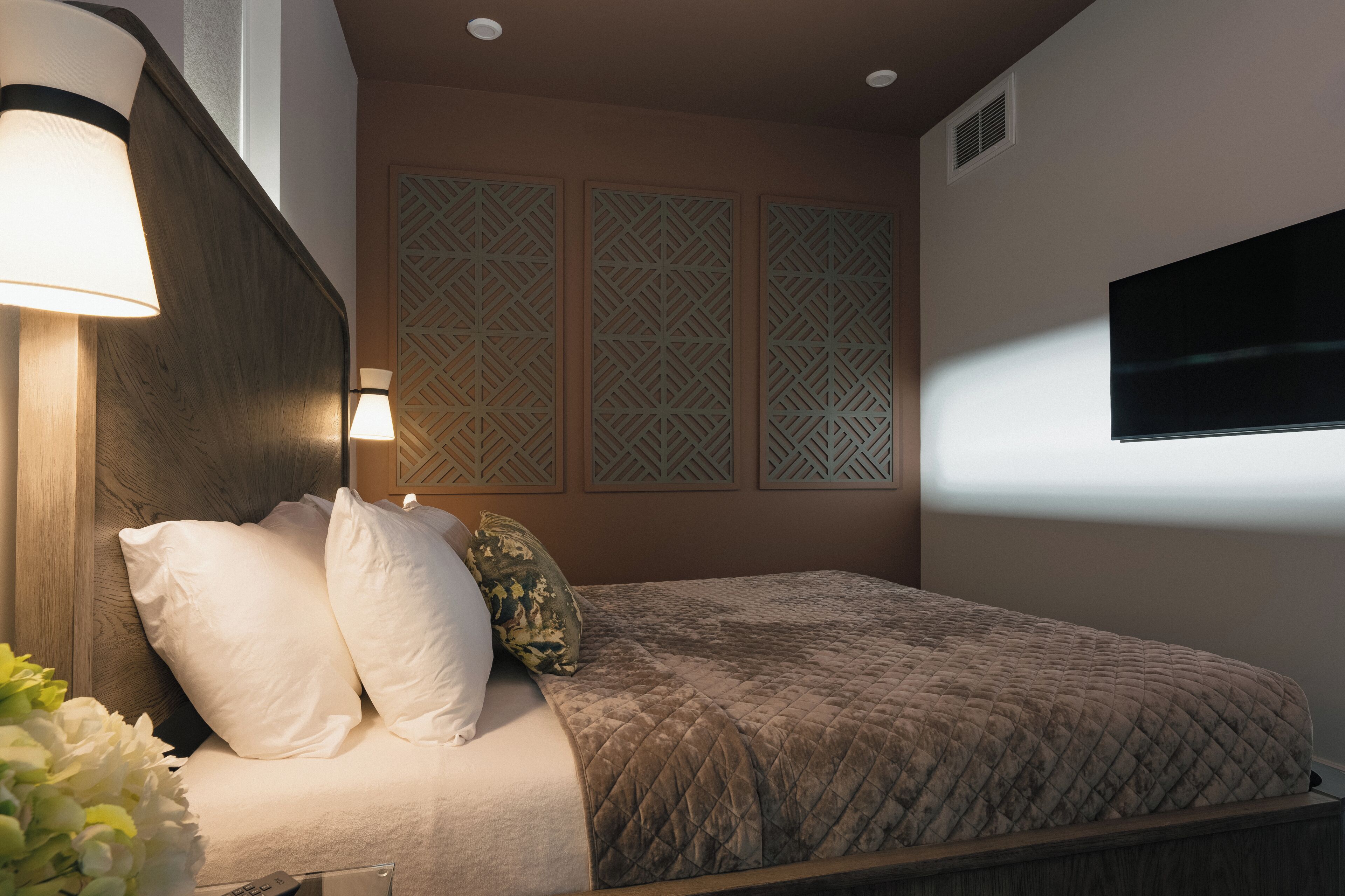 A bedroom with a bed, bedside lamps, decorative panels, and a television.