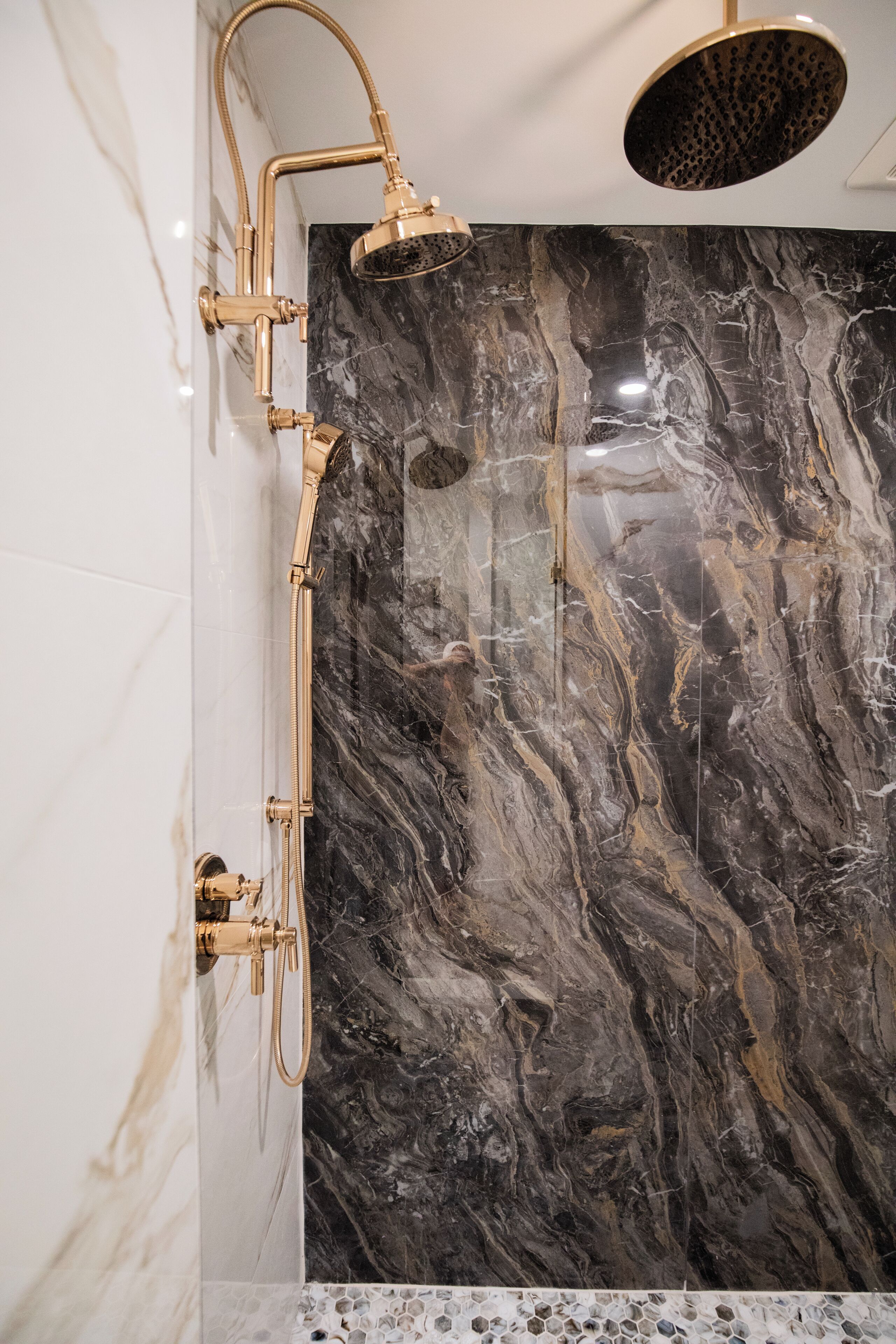 Une salle de bain avec une douche, des murs en marbre et une pomme de douche dorée.