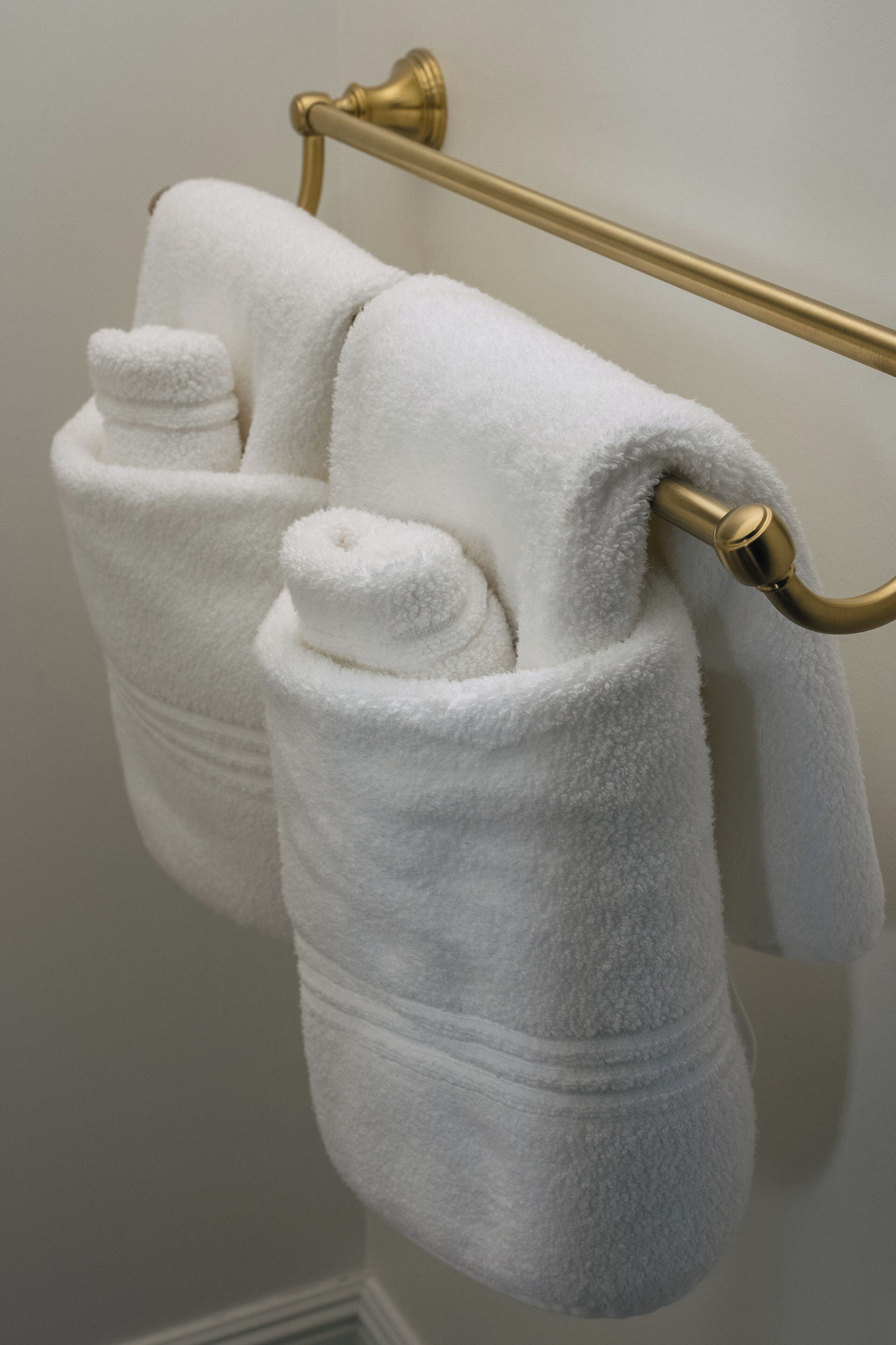 Two white towels hanging on a gold towel rack in a bathroom.