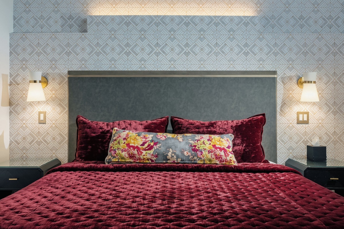 A bed with a red quilt, two pillows, and a floral throw.
