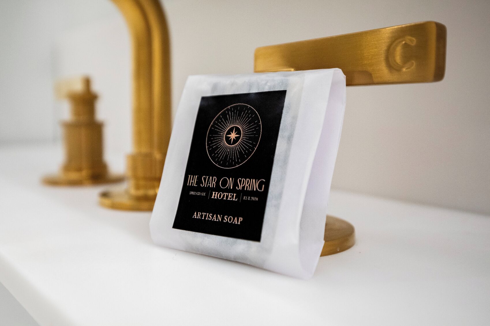 A package of artisan soap labeled 'The Star on Spring Hotel' on a white surface with a gold-colored object in the background.