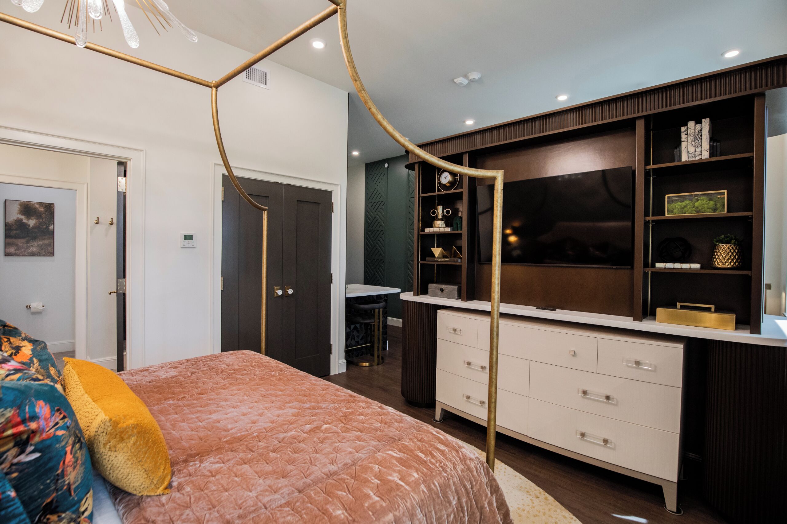 A bedroom with a four-poster bed, a dresser, a vanity, and a desk.