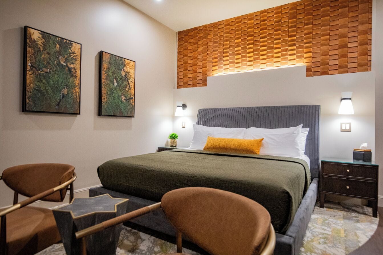 Une chambre d’hôtel comprenant un lit, deux chaises, une table de chevet et deux tableaux accrochés au mur.