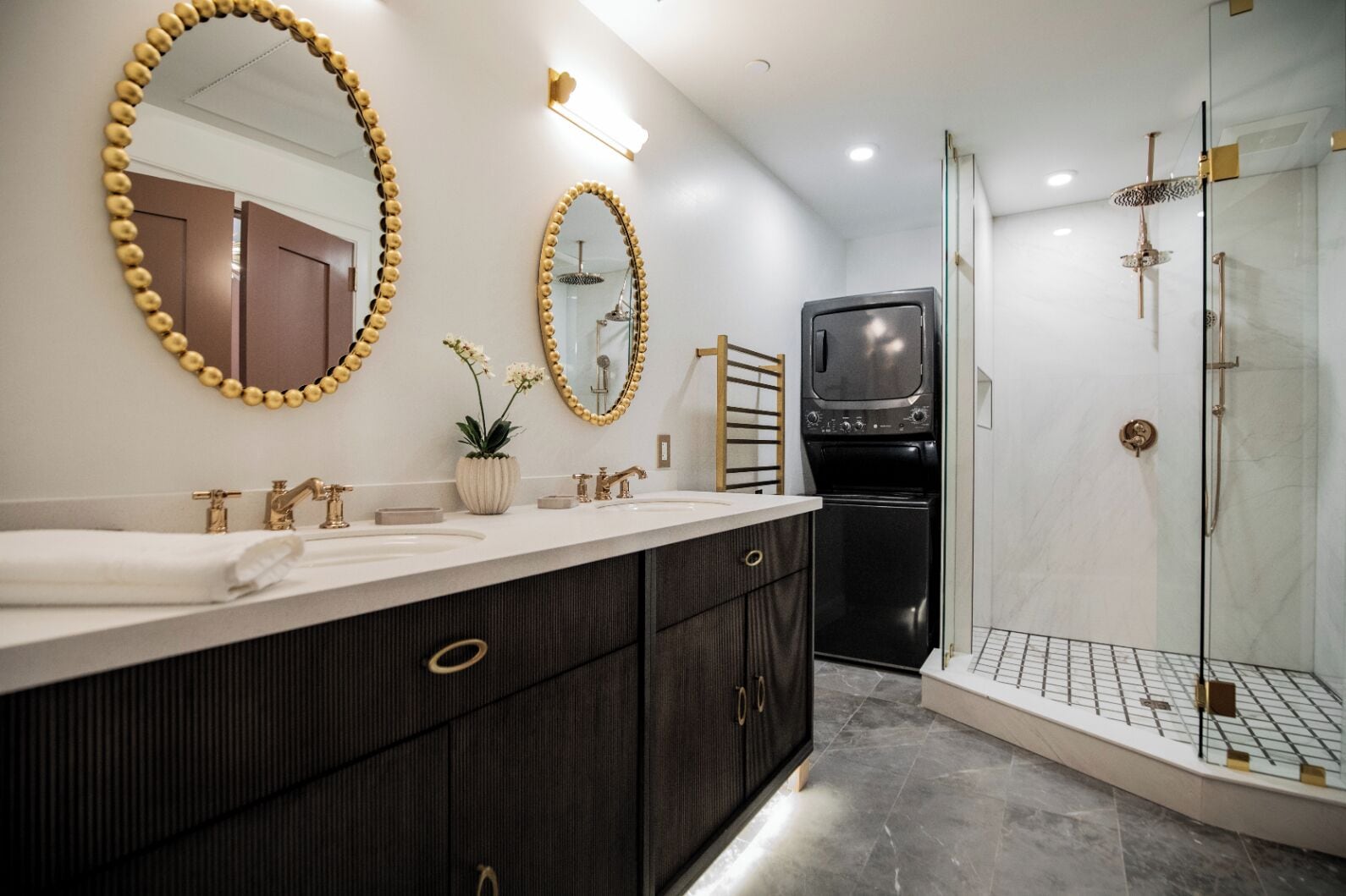 Un baño moderno con un tocador grande, dos espejos, una ducha y lavadora y secadora integradas.