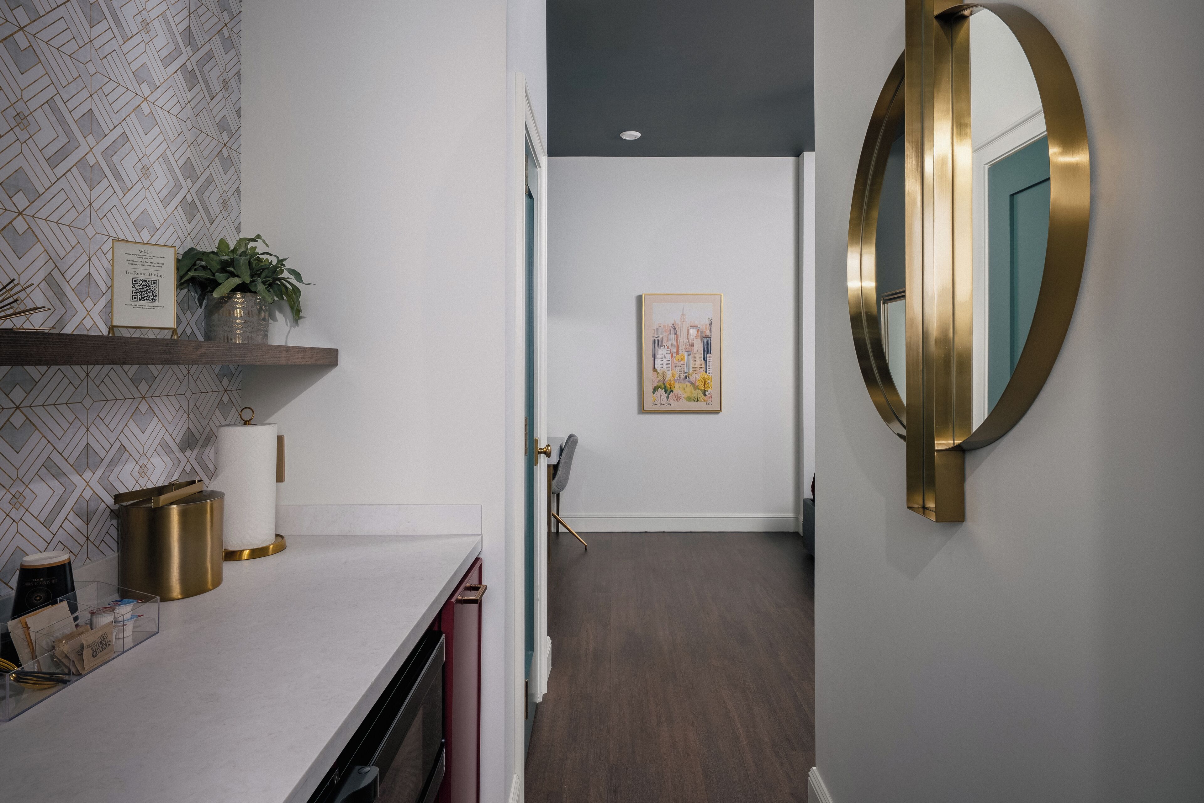 Une salle de bain moderne avec un meuble-lavabo blanc, un miroir doré et un mur orné d’un motif géométrique.