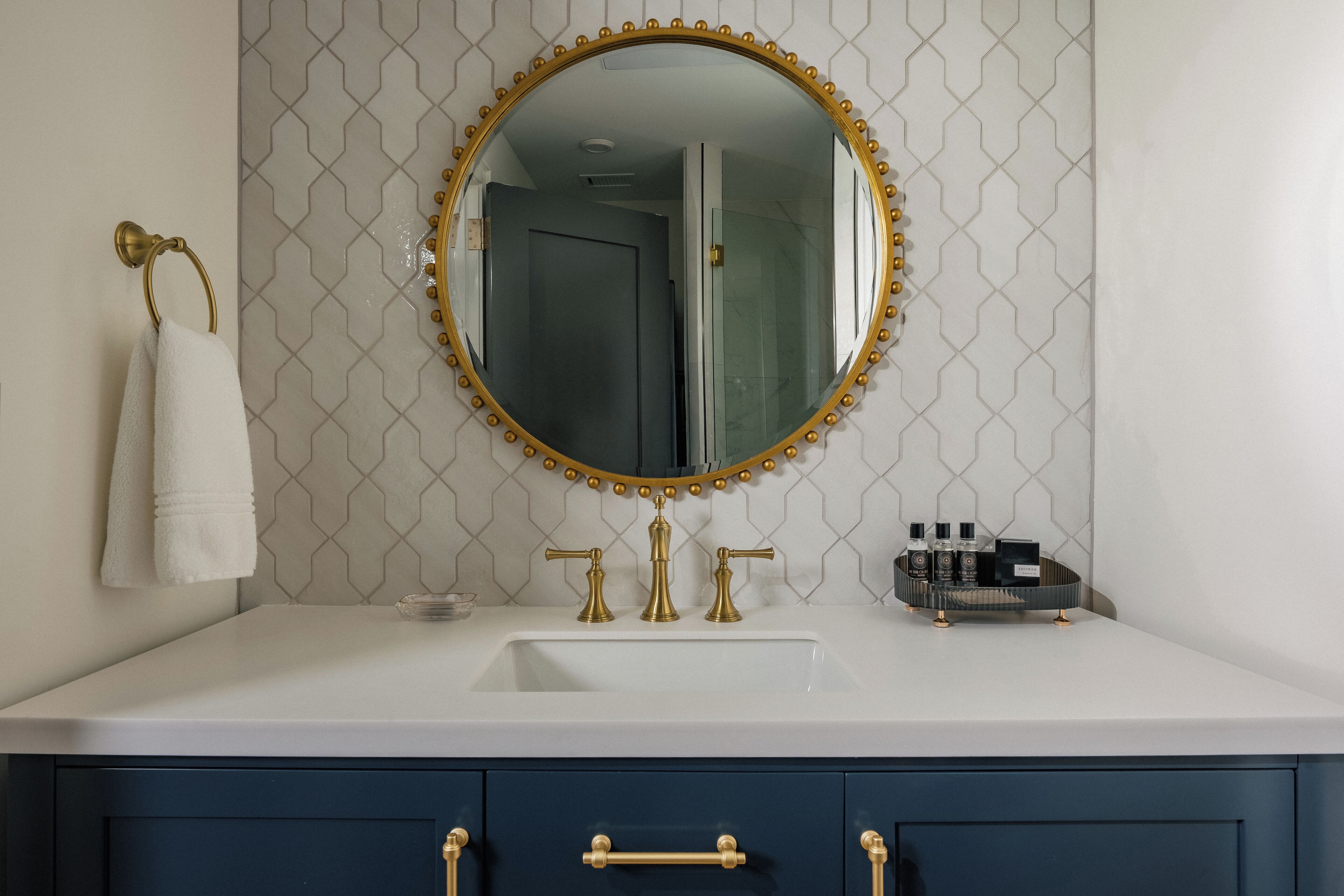 A bathroom with a white sink, gold faucets, a gold-framed mirror, and a blue cabinet.