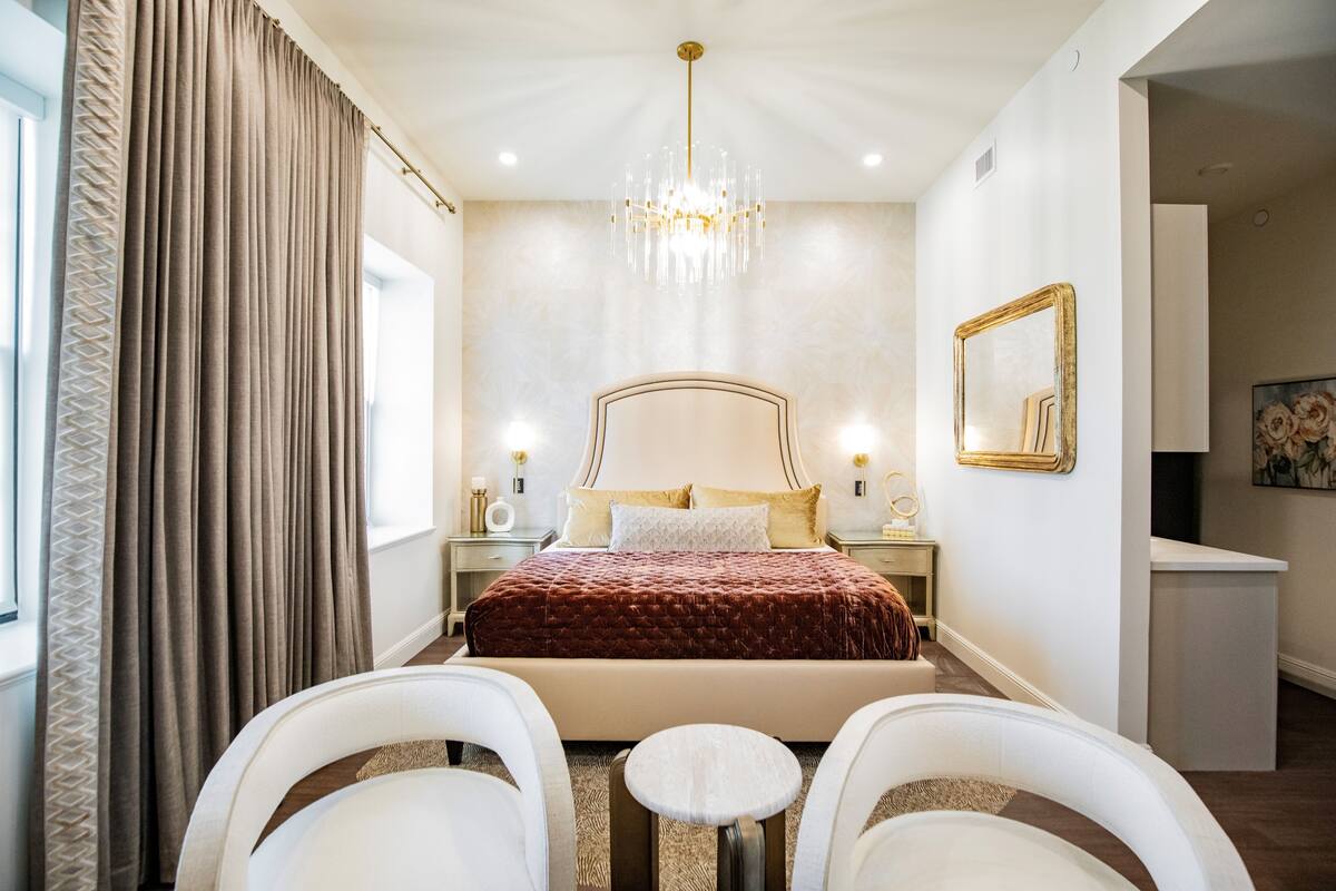 A bedroom with a large bed, bedside tables, a chandelier, and a mirror.