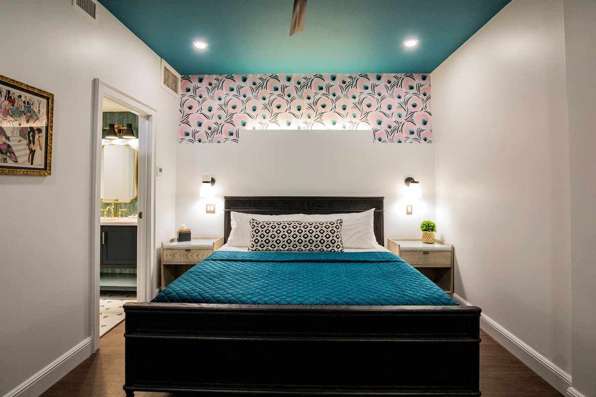 A bedroom with a bed, nightstands, a mirror, and a door leading to a bathroom.