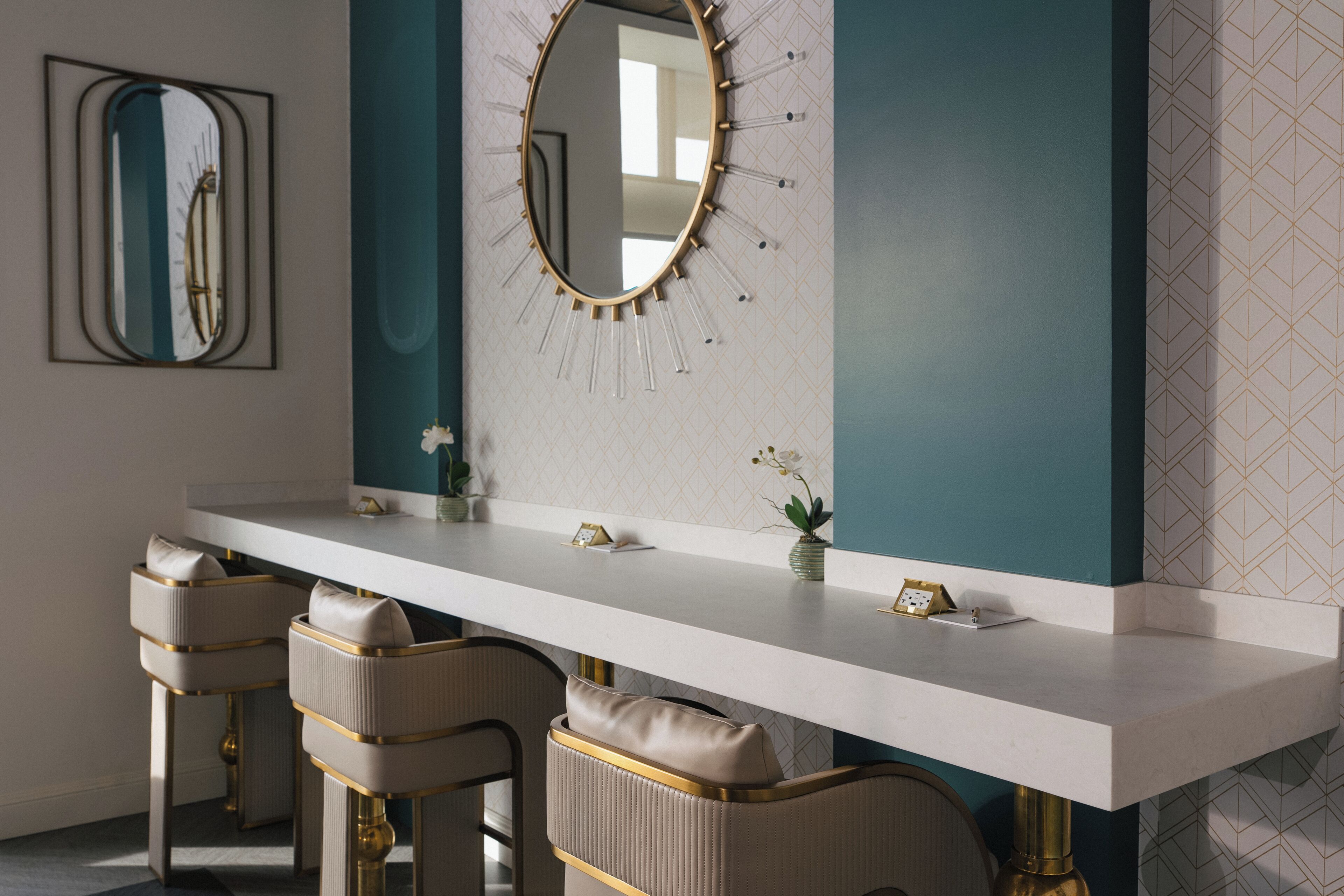 Un baño moderno con tocador blanco, detalles dorados y una pared de acento color aguamarina.