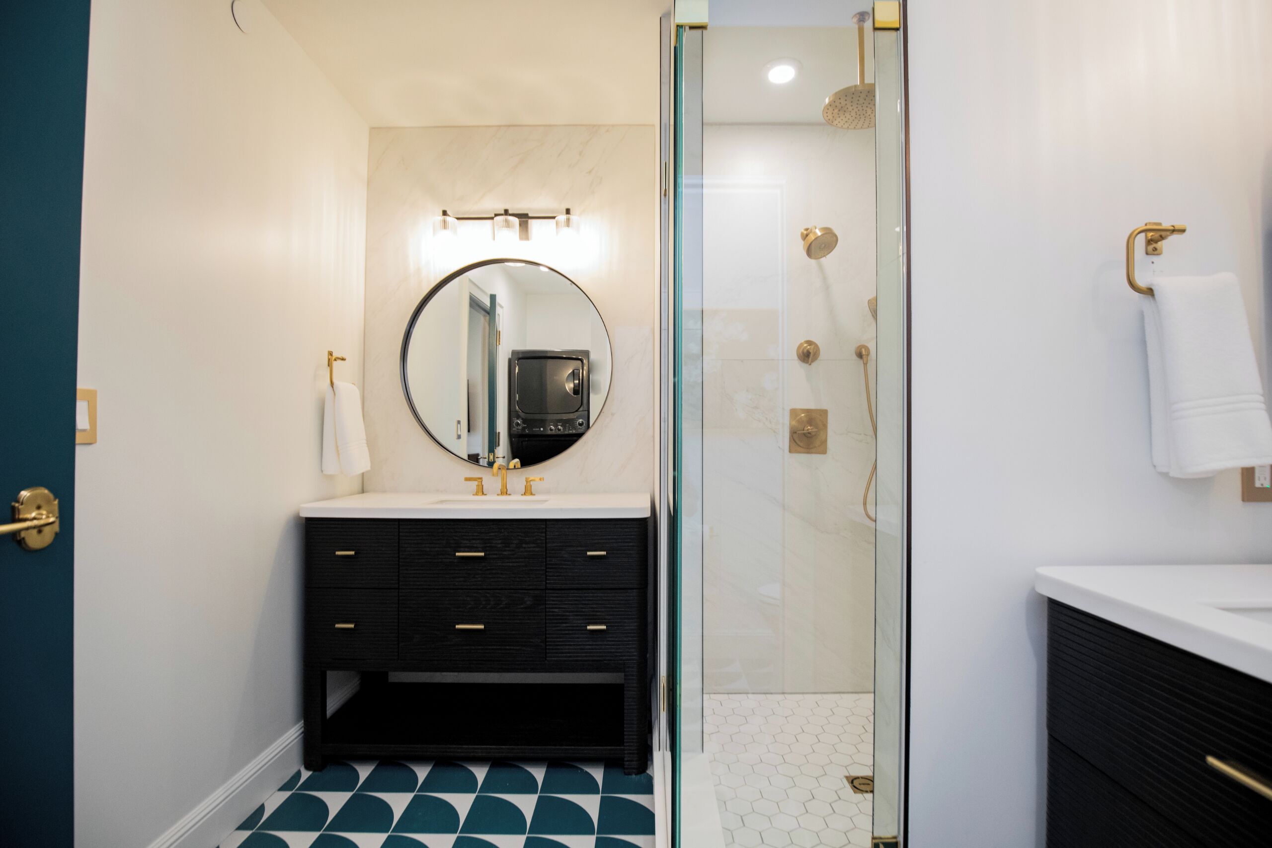 A bathroom with a glass-enclosed shower, a round mirror, a black vanity with drawers, and a white sink.