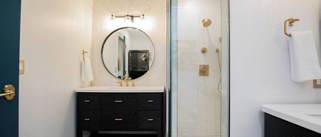 A bathroom with a glass-enclosed shower, a round mirror, a black vanity with drawers, and a white sink.