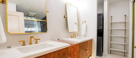 Une salle de bain moderne avec deux vasques, des robinetteries dorées et une coiffeuse avec un grand miroir.