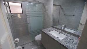 Ett modernt badrum med en dusch som är avskärmad med glasväggar, en toalett och en tvättställ med en bänkskiva i granit.