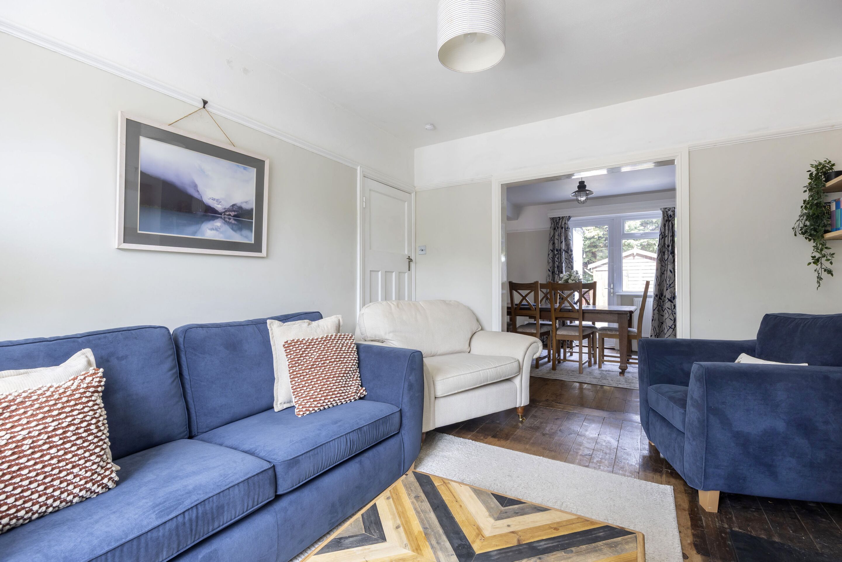 A living room with a blue sofa, a white armchair, and a dining area with a table and chairs.