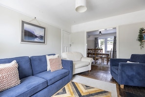 A living room with a blue sofa, a white armchair, and a dining area with a table and chairs.