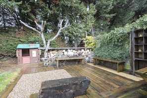 Une terrasse en bois avec un muret en pierre, une petite construction en bois surmontée d’un toit végétalisé et un banc.