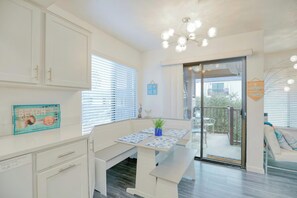 A bright kitchen with white cabinets, a dining table with blue and white placemats, and a view of the outdoor balcony. - Modern Coastal Condo in Downtown Pismo Beach | Gated Parking | Walk to Beach (Pismo Beach)