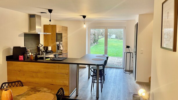 A modern kitchen with a dining area, large windows, and a view of the outdoors.