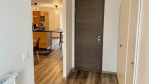 A modern kitchen with wooden cabinets, a dining area with a table and chairs, and a dark wooden door with a handle.