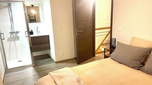 A hotel room with a bed, a bathroom with a shower, a mirror, and a wooden floor.