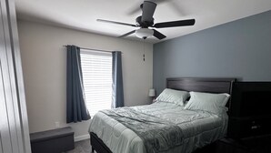 A bedroom with a bed, a ceiling fan, a window with curtains, a bedside lamp, and a nightstand. - Spacious 5-bedroom Pool Home near Beaches-Hot Tub, Kayaks, Massage Chair (North Port)