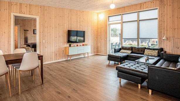 A modern living room with wooden panel walls, a flat-screen TV, a sofa set, and a dining area with a table and chairs. - Gorgeous home in Grenaa with sauna (Grenaa)