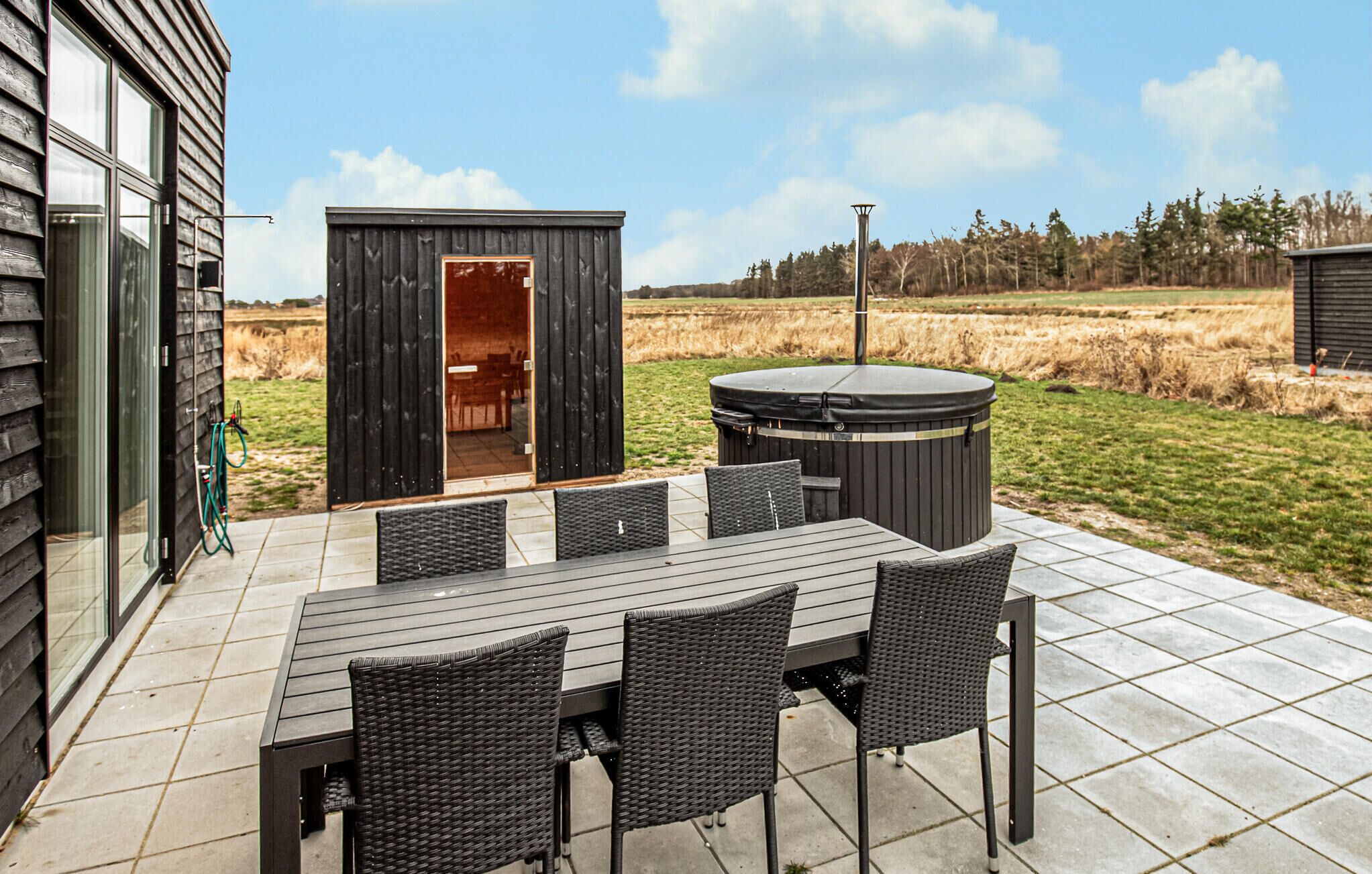 An outdoor patio with a table and chairs, a hot tub, and a wooden structure.