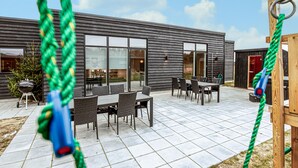 A modern building with a patio area featuring a dining table and chairs, a barbecue grill, and a swing set. - Gorgeous home in Grenaa with sauna (Grenaa)