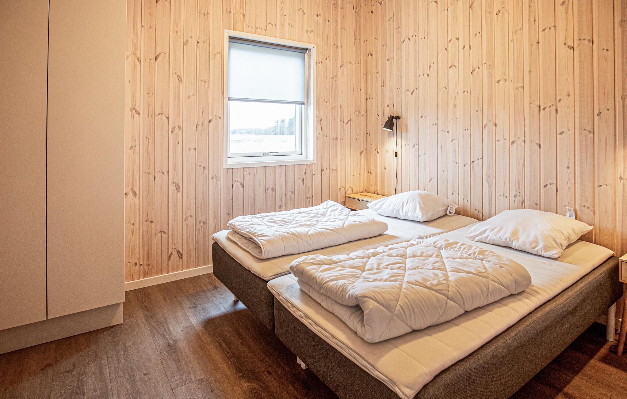 Una stanza con pareti in legno, una finestra, un letto con due cuscini, un comodino e una lampada.