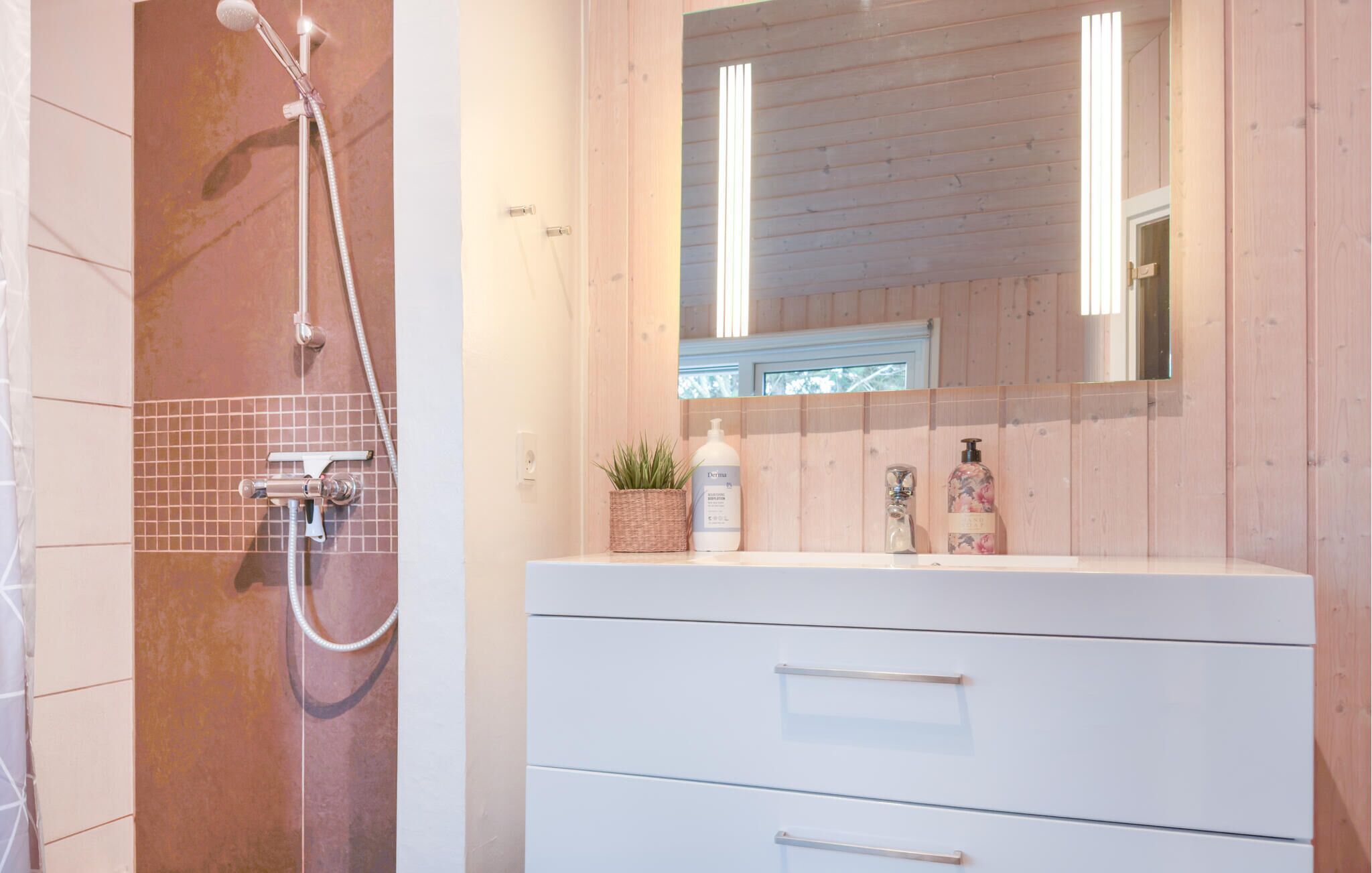 Un baño con ducha, un lavabo con espejo y una planta en maceta.