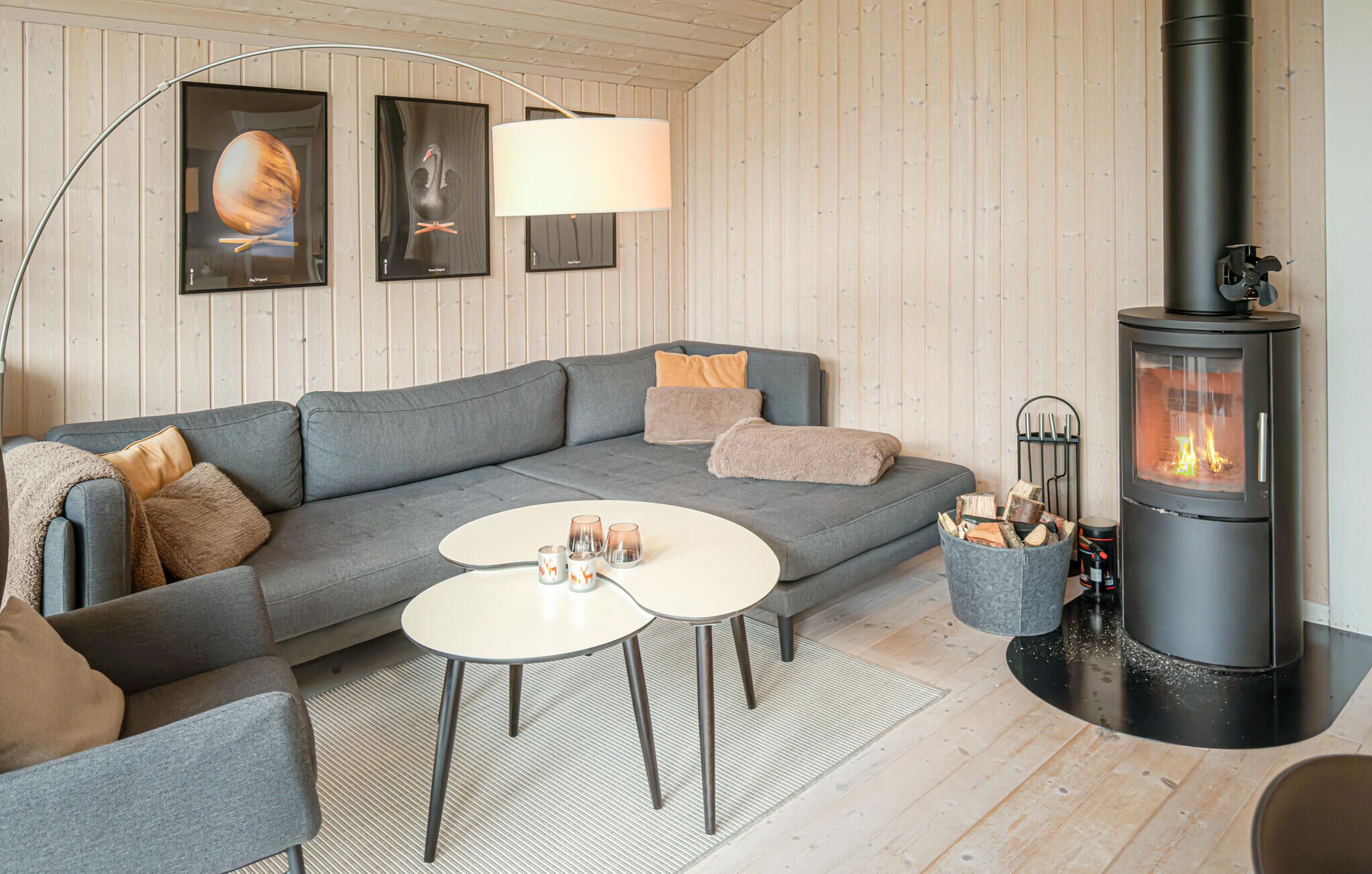 A cozy living room with a grey sofa, two white coffee tables, a black wood-burning stove, and framed artwork on the wall.