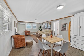 Une pièce chaleureuse avec une table à manger en bois, des chaises blanches, un canapé beige, des meubles en osier et un meuble blanc.