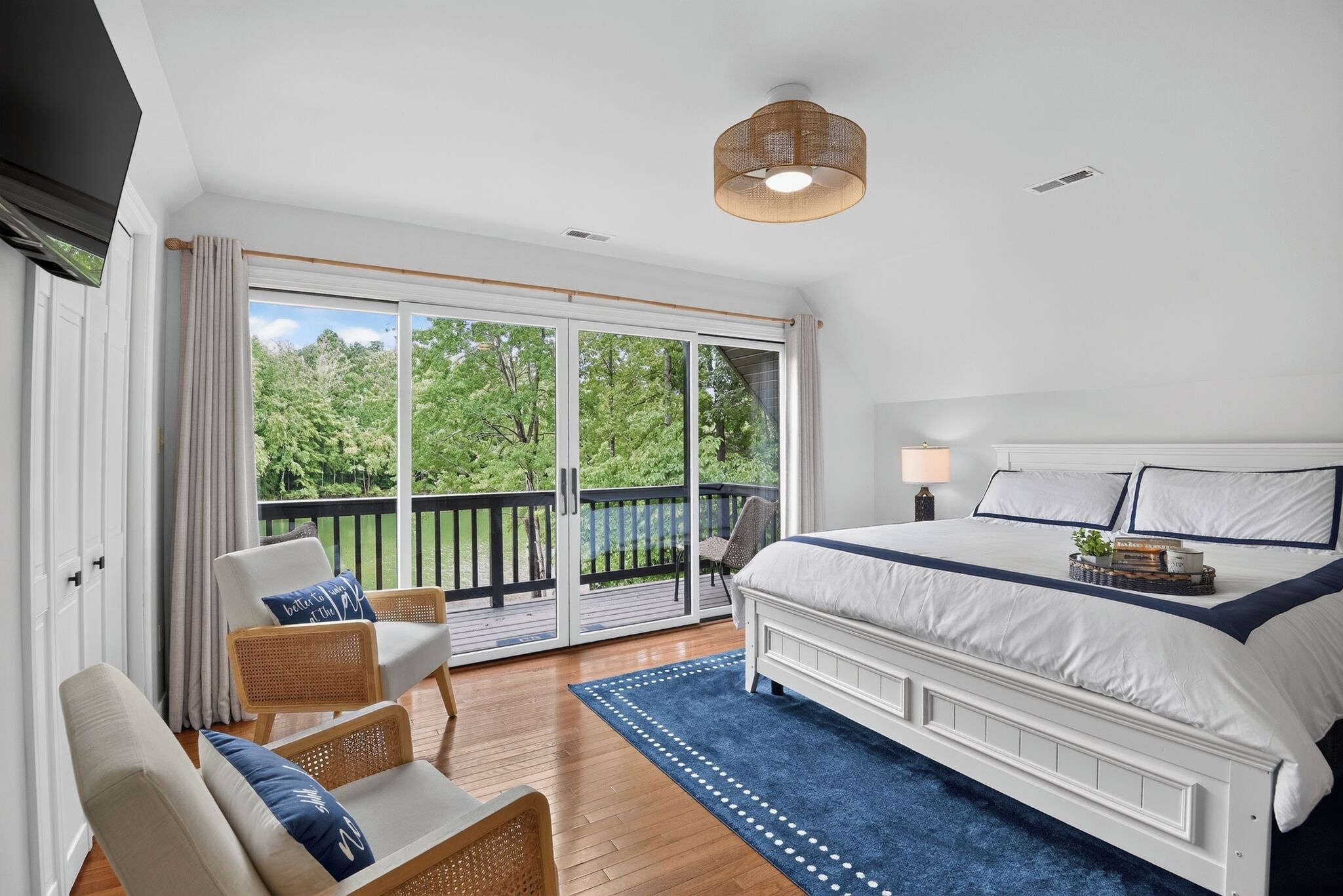 A bedroom with a large bed, a balcony with a view of trees, and a ceiling light fixture.