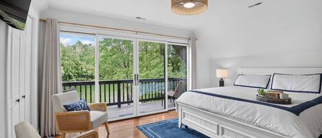 A bedroom with a large bed, a balcony with a view of trees, and a ceiling light fixture.