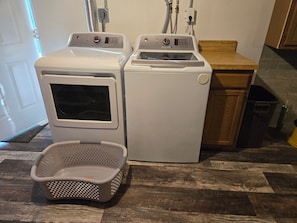 A laundry room with two stacked washers and dryers, a laundry basket, and a wooden cabinet.