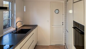 Eine Küche mit schwarzem Arbeitsplatz, einem Spülbecken, einem Fenster und einer Tür mit rundem Fenster.