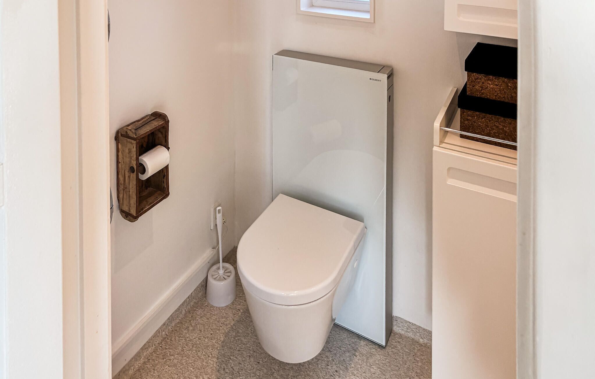 Et lille, moderne badeværelse med toilet, toiletpapirsholder og en håndtørrer.
