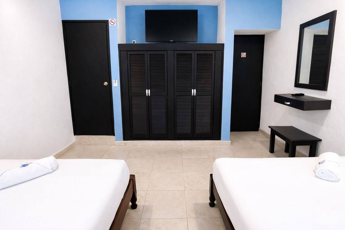 Une chambre d’hôtel avec deux lits, une télévision, une armoire et une petite table.