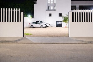 Un camino de entrada cerrado por una reja que conduce a un edificio de fachada blanca y varias ventanas.