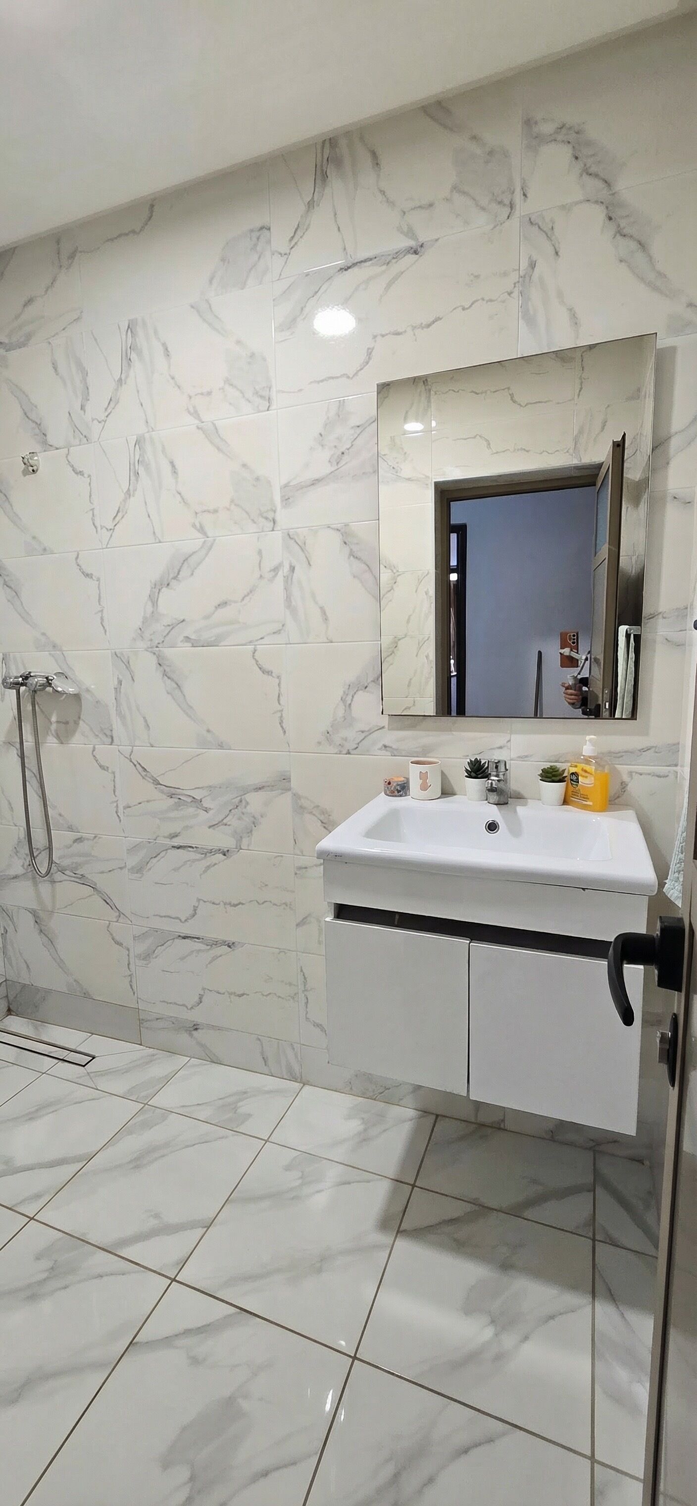 A bathroom with marble tiles, a sink, a mirror, and a shower.