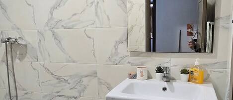 A bathroom with marble tiles, a sink, a mirror, and a shower.