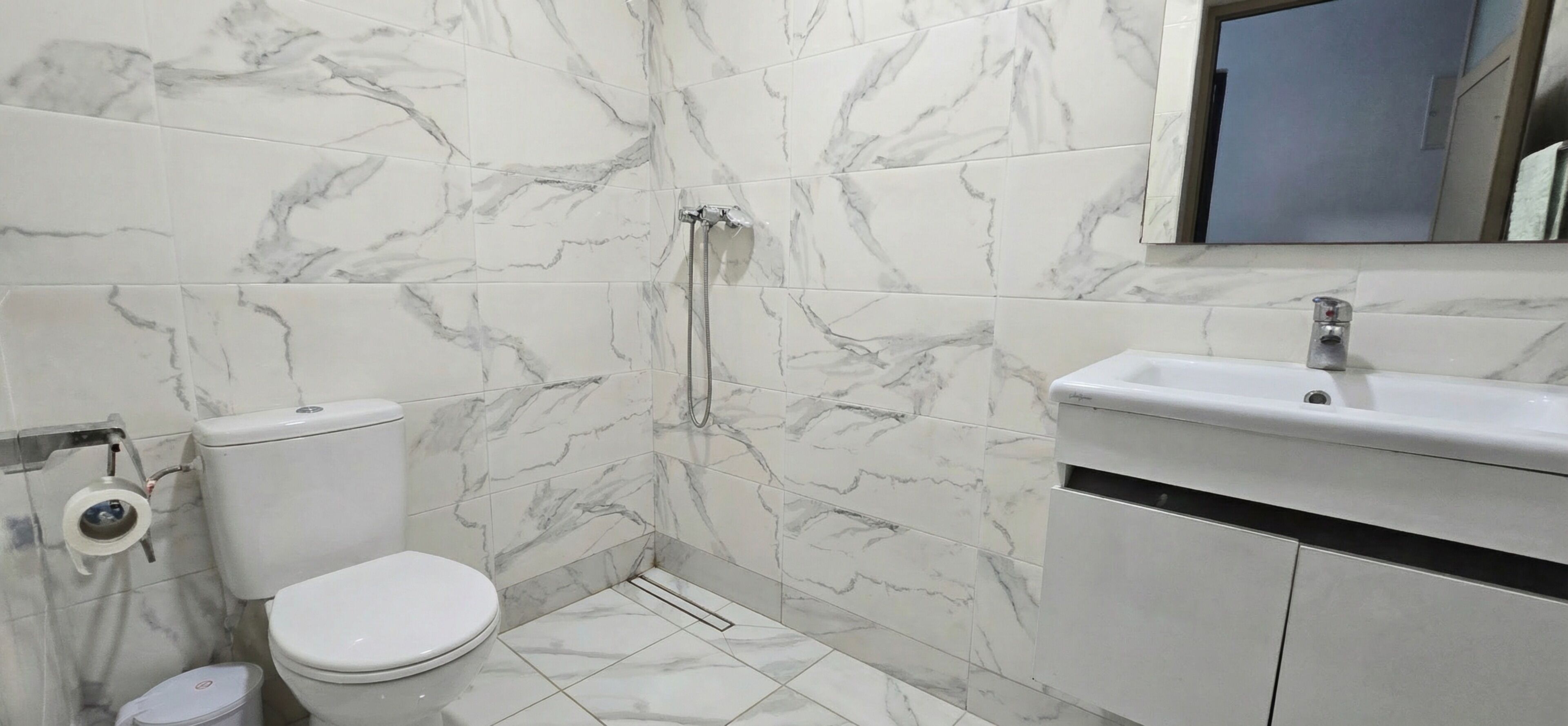 Une salle de bain équipée de toilettes, d’une douche, d’un lavabo et de carreaux de marbre.