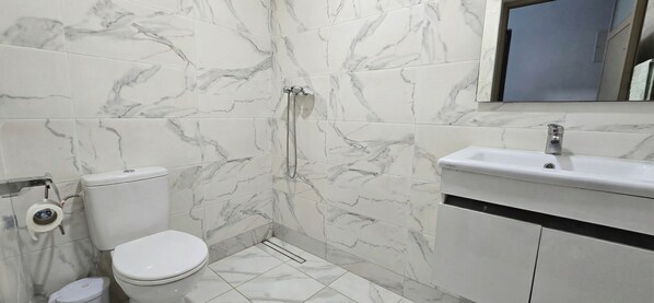 Un baño con inodoro, ducha, lavamanos y azulejos de mármol.