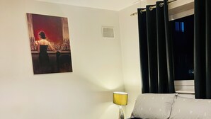 A hotel room with a bed, a nightstand, a lamp, a window with curtains, and a wall-mounted picture. - The Luxe Loft Apartment. (Wolverhampton)