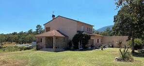 Ein zweistöckiges Haus mit Naturstein-Fassade, Ziegeldach und einer kleinen Terrasse mit Gartenmöbeln.