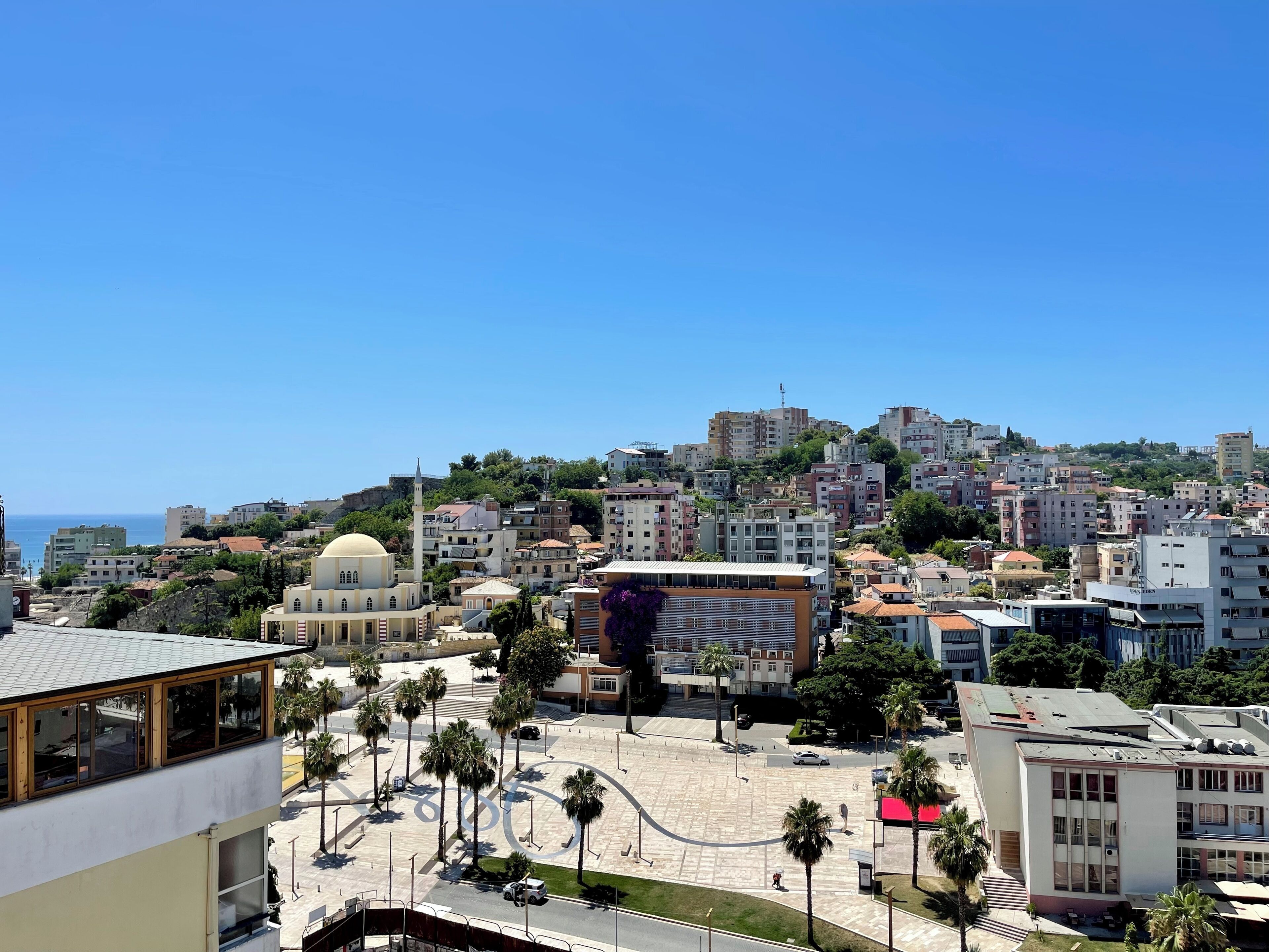 A cityscape with a prominent mosque, modern buildings, and a clear blue sky.
